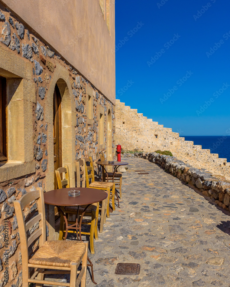 Traditional cafe exterior in the fortified medieval  castle of Monemvasia. Iron tables and wooden chairs  with the view of the  aegean sea in the background.