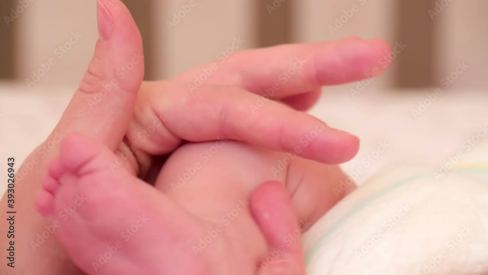 Favorite Small Heels. Newborn baby in a diaper lying on the changing table. Female hand gently stroking baby legs Favorite Small Heels. Newborn baby in a diaper lying on the changing table. Female hand gently stroking baby legs