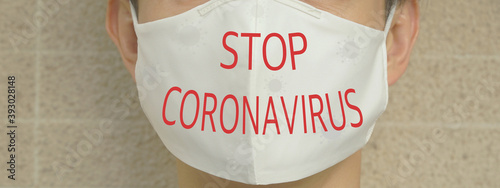 Young man wearing white cotton face mask with red word “Stop Coronavirus”.