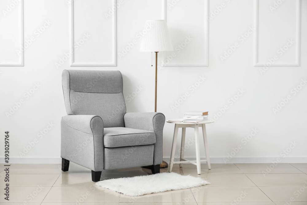 Stylish armchair with table, books and lamp near light wall in room Stylish armchair with table, books and lamp near light wall in room