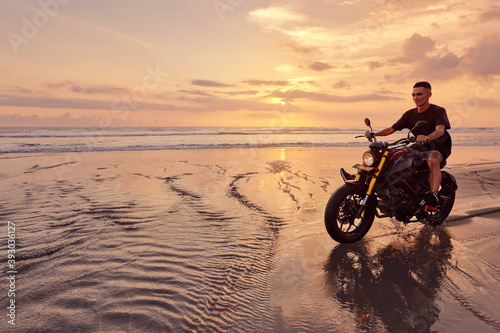 Man And Motorcycle On Ocean Beach At Beautiful Tropical Sunset. Handsome Biker On Motorbike On Sandy Coast In Bali  Indonesia.