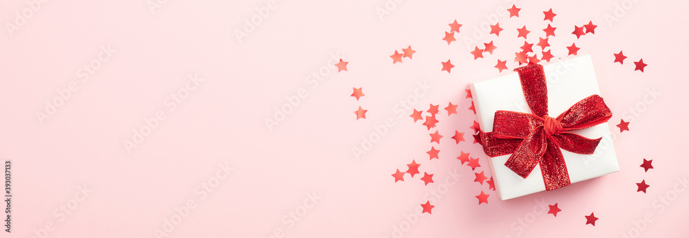White gift box with red ribbon bow and confetti stars on pastel pink background. Christmas present, valentine day surprise, birthday concept. Flat lay, top view. White gift box with red ribbon bow and confetti stars on pastel pink background. Christmas present, valentine day surprise, birthday concept. Flat lay, top view.