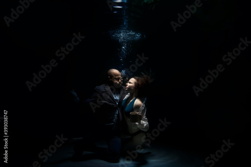 Young businessman embrace his woman, looks into her eyes, kisses beloved, underwater. Emotional happy couple in pond. Concept romantic, surprise and commitment to development relations. Copy space