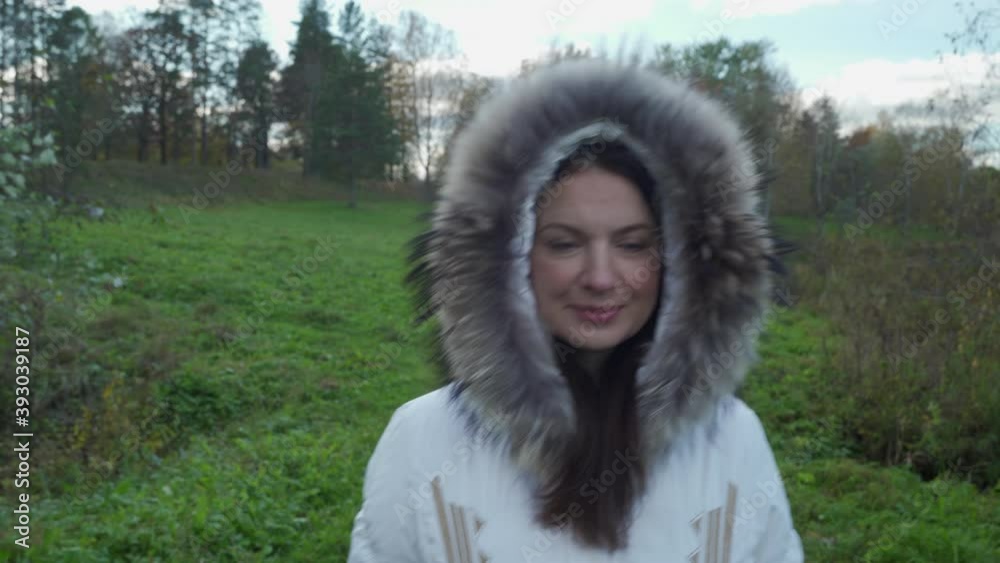 Beautiful woman with brown hair walking in park on cold autumn day with trees covered in yellow leaves in warm fur collar coat Beautiful woman with brown hair walking in park on cold autumn day with trees covered in yellow leaves in warm fur collar coat