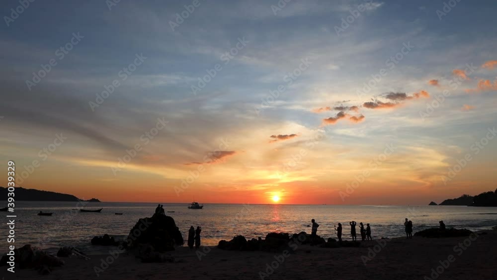Small silhouettes of people on the background of a beautiful orange sunset on the coast of Phuket island Small silhouettes of people on the background of a beautiful orange sunset on the coast of Phuket island