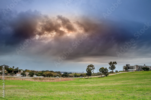 View of  Table Mountain covered in clouds at sunset with a lake and green lawn in foreground, Cape Town, South Africa