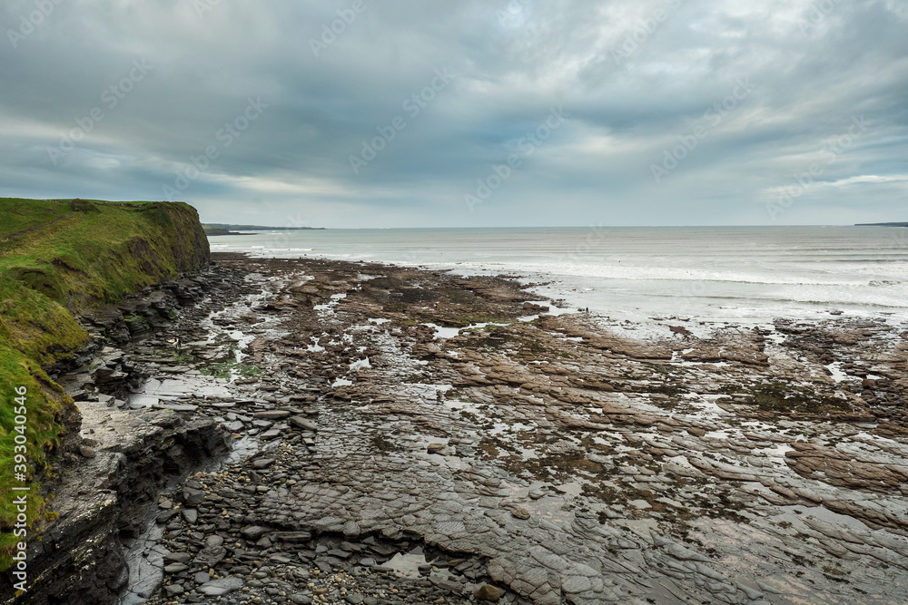 Rough stone ocean bed exposed at low tide, blue cloudy sky. Atlantic ocean, Lahinch, county Clare, Ireland.