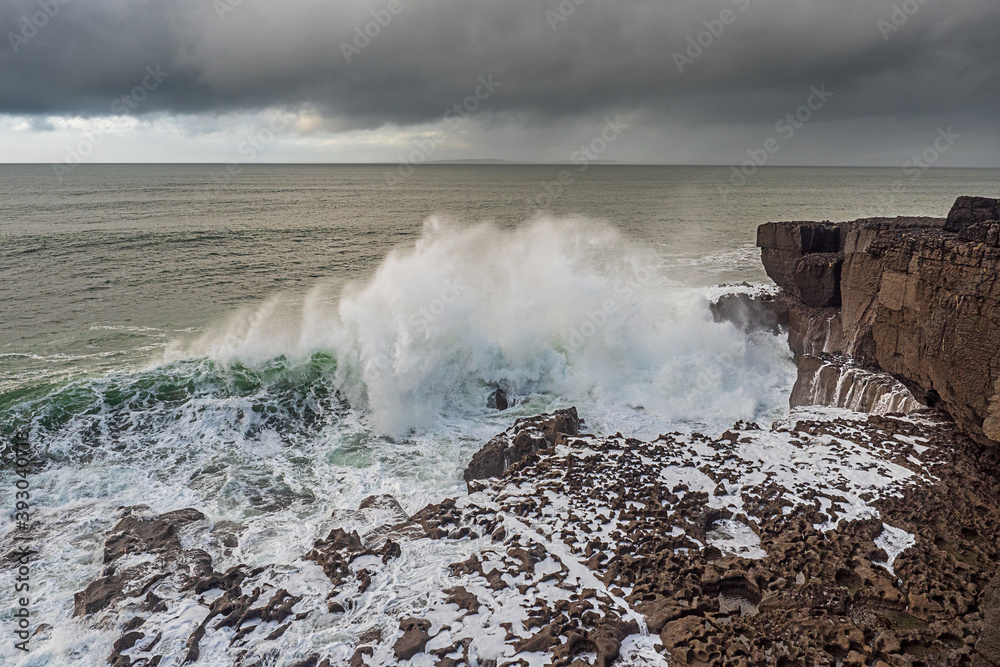 Powerful waves hit the rough stone coast line creating huge splashes of water. Low dark storm clouds, West of Ireland. Nobody.