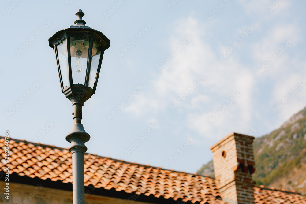 High street lamp at the level of the roof of the house against the background of mountains and sky.