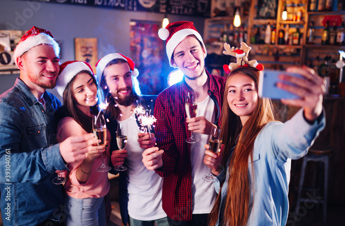 Smiling friends with glasses of champagne and phone taking selfie in club. Group of young people having fun with sparkles. Party, holidays, technology, nightlife, holidays. Christmas, New year.