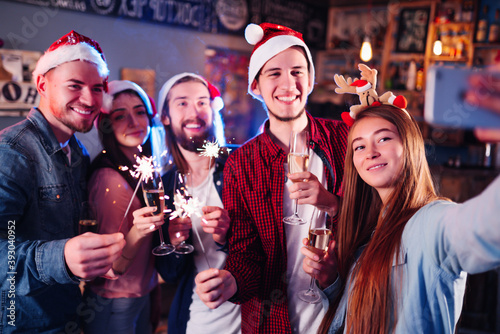 Smiling friends with glasses of champagne and phone taking selfie in club. Group of young people having fun with sparkles. Party, holidays, technology, nightlife, holidays. Christmas, New year.