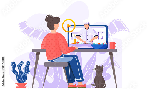 A girl with a cat is sitting at a computer monitor on an online cooking lesson. A male chef on the screen prepares a salad while streaming for master class via the Interner. Video about recipes