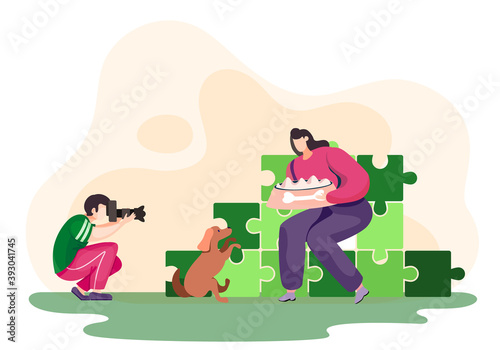 Professional photographer shooting outdoor session with the camera. Beautiful woman feed her dog, while young man tries to capture it. Photo session in the park with puzzles on the background