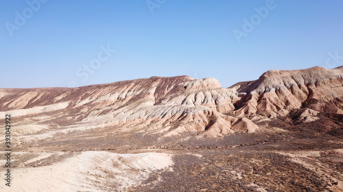 Colored hills of the gorge in the desert. Top view from drone of the red-orange-yellow hills. Cut in different layers  like epochs. Clay of the mountain. Low dry bushes  cracks  blue sky. Kazakhstan.