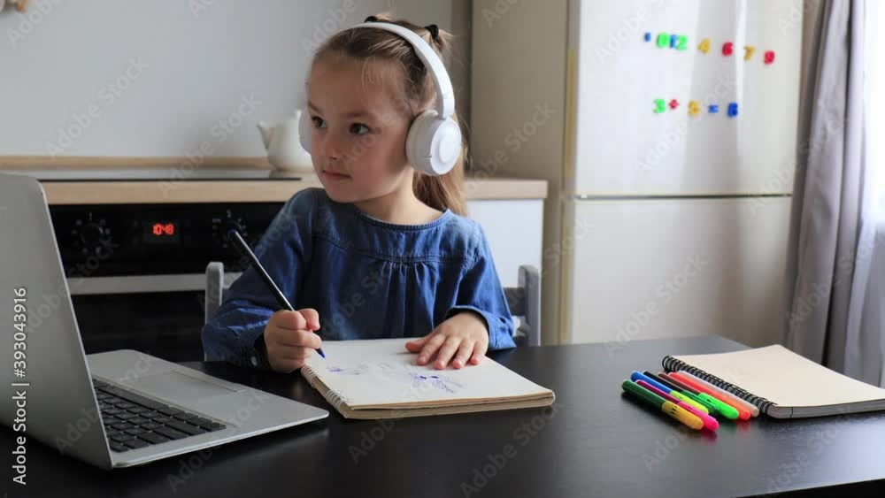 Smart small preschooler girl in headphones handwrite online using laptop at home, little child in earphones study on Internet using pc wireless connection Smart small preschooler girl in headphones handwrite online using laptop at home, little child in earphones study on Internet using pc wireless connection