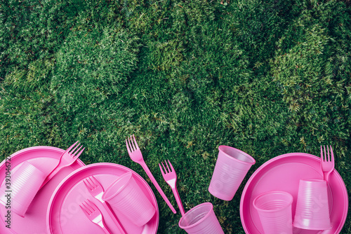 Recycling plastic and ecology. Disposable plastic tableware - plates, forks, spoons, knives. Top view. Copy space. Environmental pollution. Pink plastic waste on green grass, moss background