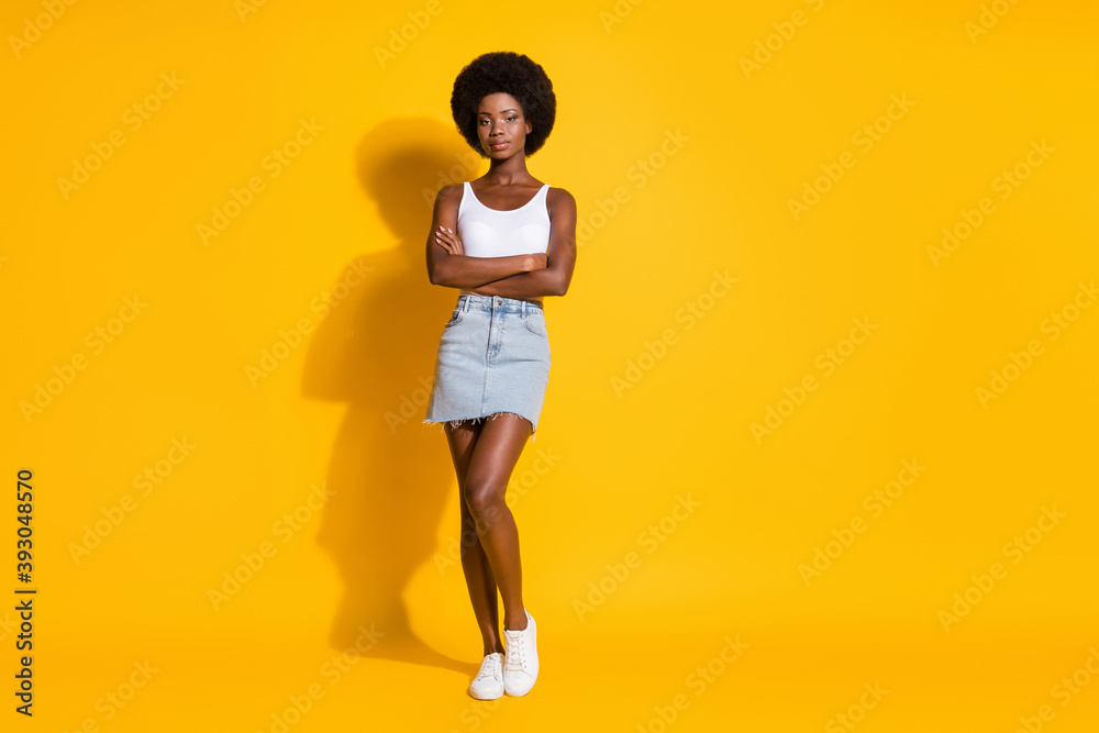 Photo of lovely cool black young girl crossed hands wear white singlet jeans mini skirt sneakers isolated yellow color background