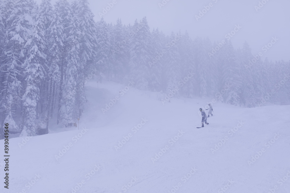 Couple of snowboarders rush downhill through a foggy ski slope