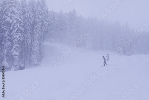 Couple of snowboarders rush downhill through a foggy ski slope