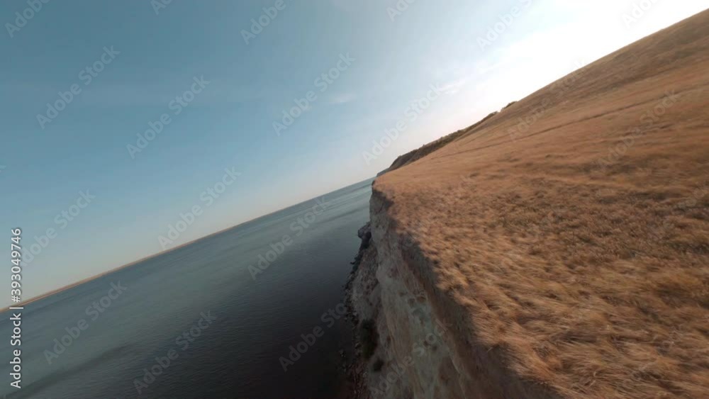 Sharp cliff on Volga river bank from cinematic fpv drone. Aerial shooting from flying drone over empty field on top cliff edge, wild lake and skyline background.