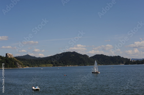 Blue waters of Czorsztyn dam lake with yacht and green hills and mountains and blue sky with clouds in summer in southern Poland