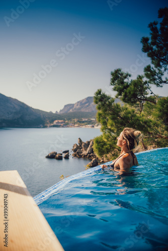 Beautiful girl on the edge of the pool, behind a beautiful spectacular view of the sea and mountains © komokvm