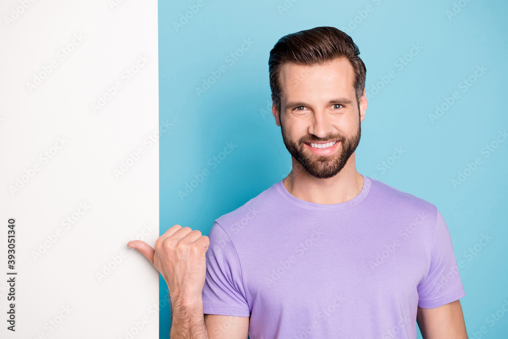 Photo portrait of bearded hipster pointing at blank white wall promotion ads smiling isolated on bright blue color background copyspace Photo portrait of bearded hipster pointing at blank white wall promotion ads smiling isolated on bright blue color background copyspace