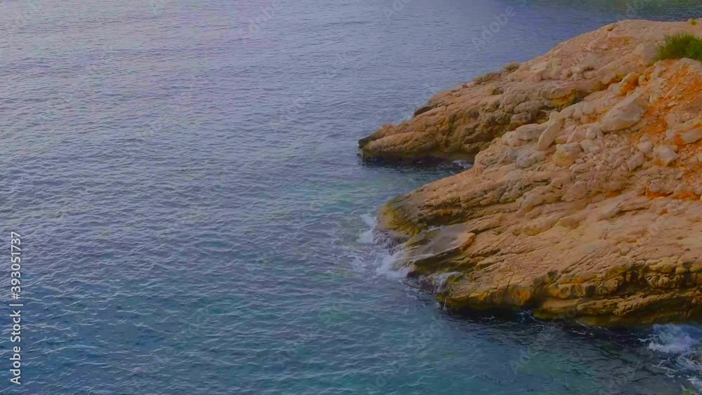 Drone camera with top view and bird's eye view. It flies over a rocky coastline. A turquoise Mediterranean Sea waves crashing against the cliffs and bubbling Drone camera with top view and bird's eye view. It flies over a rocky coastline. A turquoise Mediterranean Sea waves crashing against the cliffs and bubbling