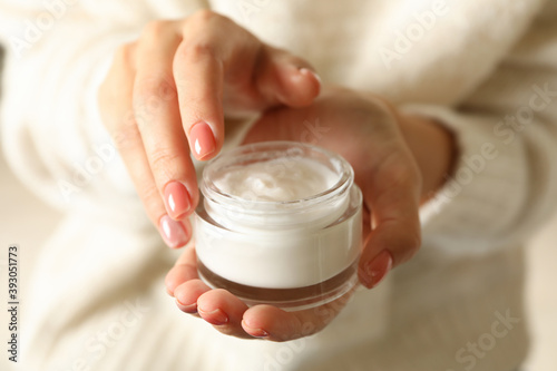 Woman in sweater with pink manicure hold jar of cosmetic cream photo