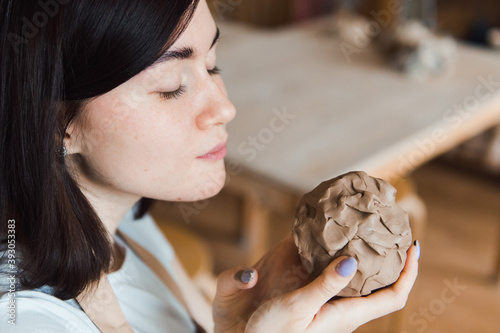 Close up portrait of young woman artisan with piece of clay in pottery workshop