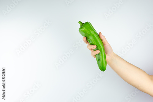 Woman's arm holding a green pepper on a white background
