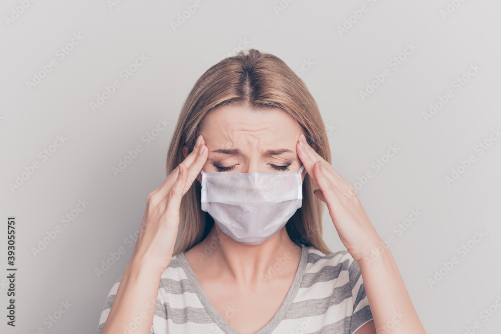 Photo portrait of woman touching temples with hands wearing white face mask isolated on grey colored backround Photo portrait of woman touching temples with hands wearing white face mask isolated on grey colored backround