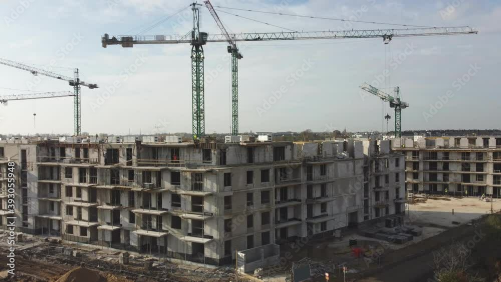 Aerial Flight Over a New Constructions Development Site with High Tower Cranes Building Real Estate. Heavy Machinery and Construction Workers are Employed. Top Down View at Contractors in Safety Hats.