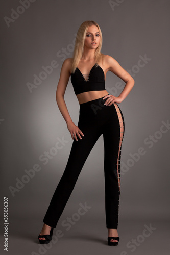 beautiful young slender blonde girl in black stylish skinny pants and a short T-shirt with an open belly on a gray background