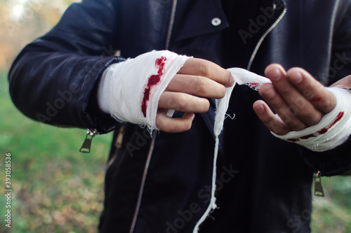 Man with bandage with blood on the knuckles, natural background. End of fight, fight, blood and aggression concept. A man in a leather jacket.