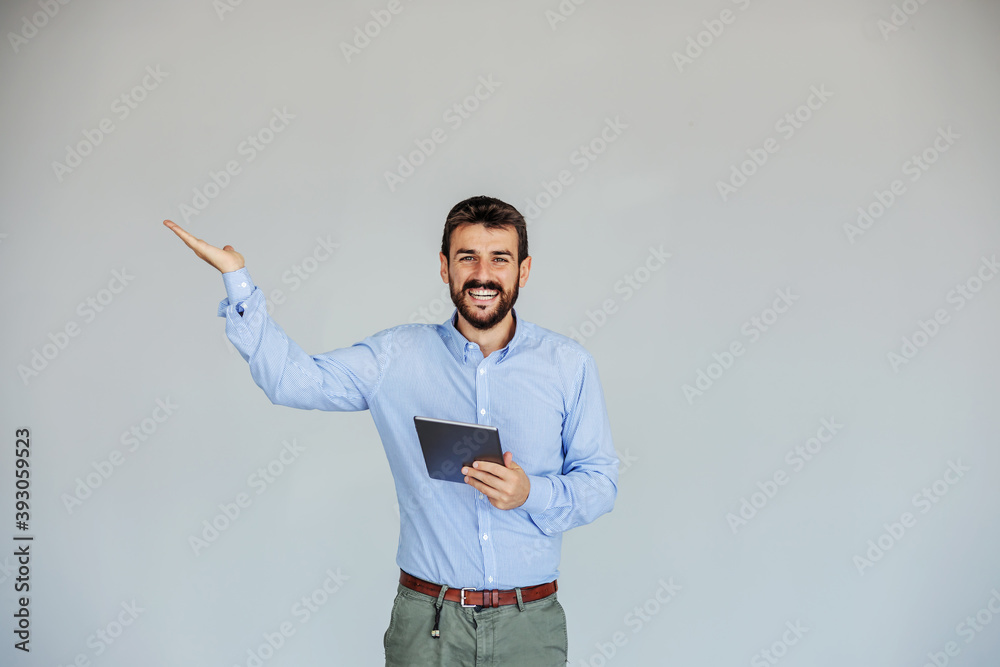 Smiling businessman standing, holding tablet and holding hand like he is showing something. Smiling businessman standing, holding tablet and holding hand like he is showing something.