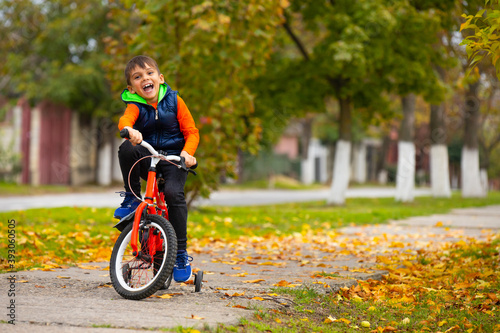 Boy on a bike ride in the autumn park. Happy smiling child cycling outdoors. Active lifestyle, hobby. Photo with empty side space