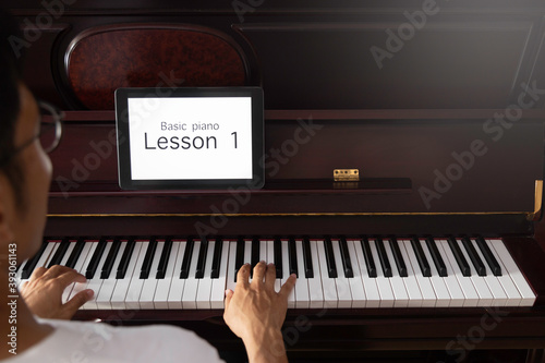 young Asian man learning basic of classic piano online by tablet at home. photo