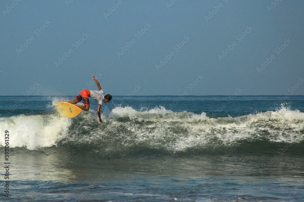 Young adults catching waves surfing at west coast Pangandaran on a bright warm sunny day on clear blue water