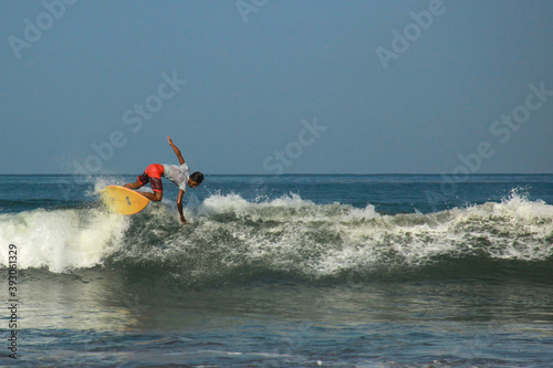 Young adults catching waves surfing at west coast Pangandaran on a bright warm sunny day on clear blue water photo