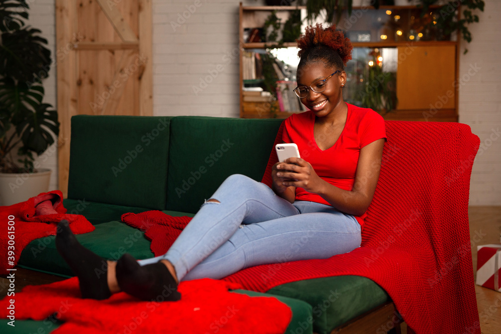 Obraz premium beautiful young african female sitting with mobile phone on the sofa