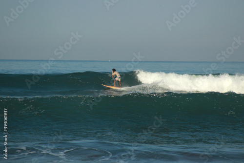 Young adults catching waves surfing at Pangandaran beach on a cloudy day on clear blue water