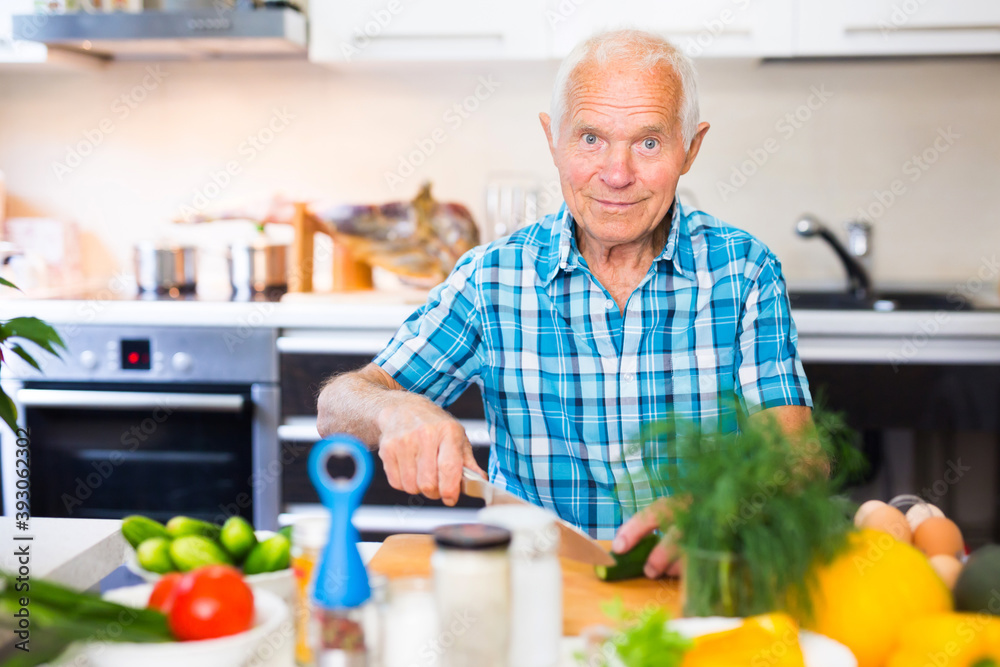 elderly man cuts vegetables for salad at the table in the kitchen elderly man cuts vegetables for salad at the table in the kitchen