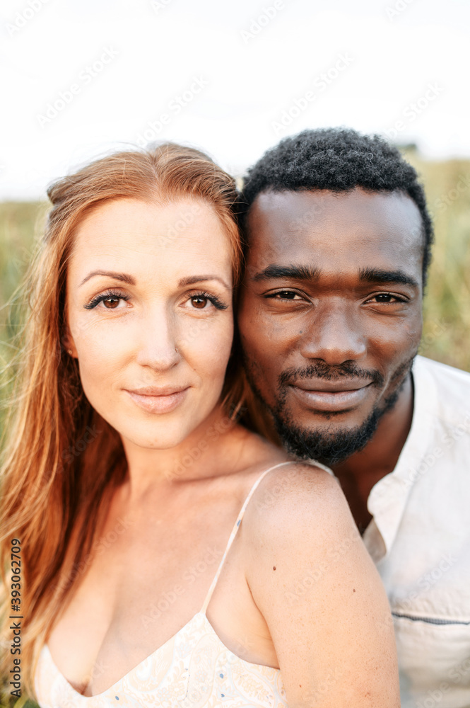 Multiracial couple in love in sunset light. Side by side a charming red haired woman with freckles and an african-american man Multiracial couple in love in sunset light. Side by side a charming red haired woman with freckles and an african-american man