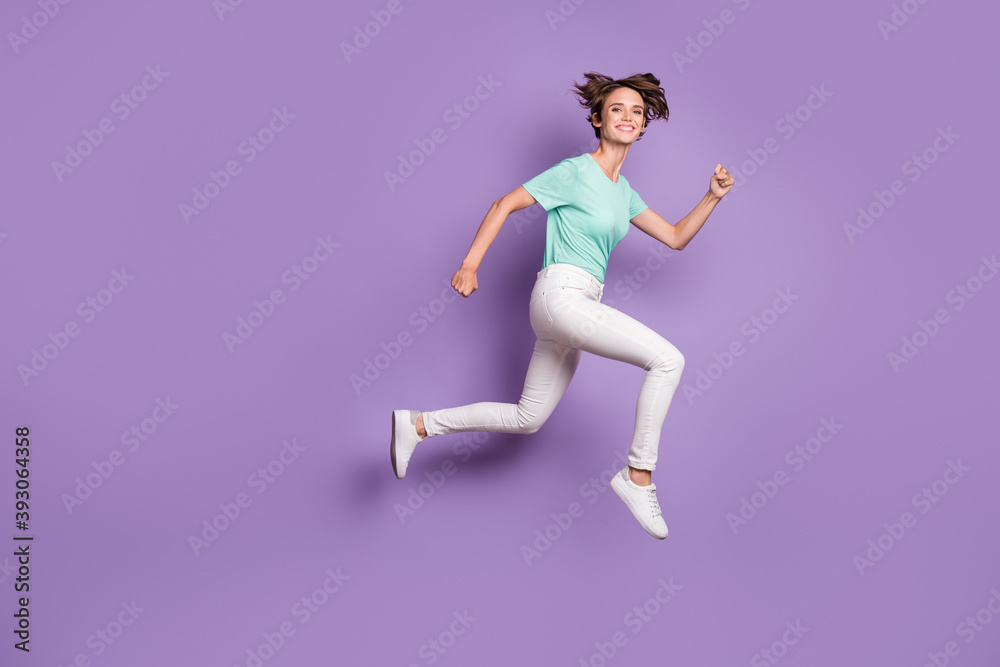 Full size profile photo of sweet optimistic girl jumping hands fists wear white sneakers trousers blue t-shirt isolated on violet background