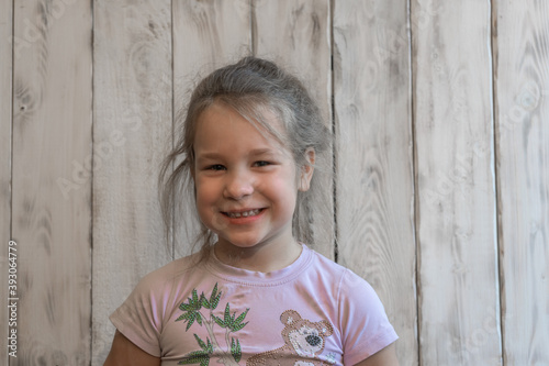Little girl posing in front of the camera, smiling, wooden photo background, in a pink t-shirt with a bear. Warm pastel colors