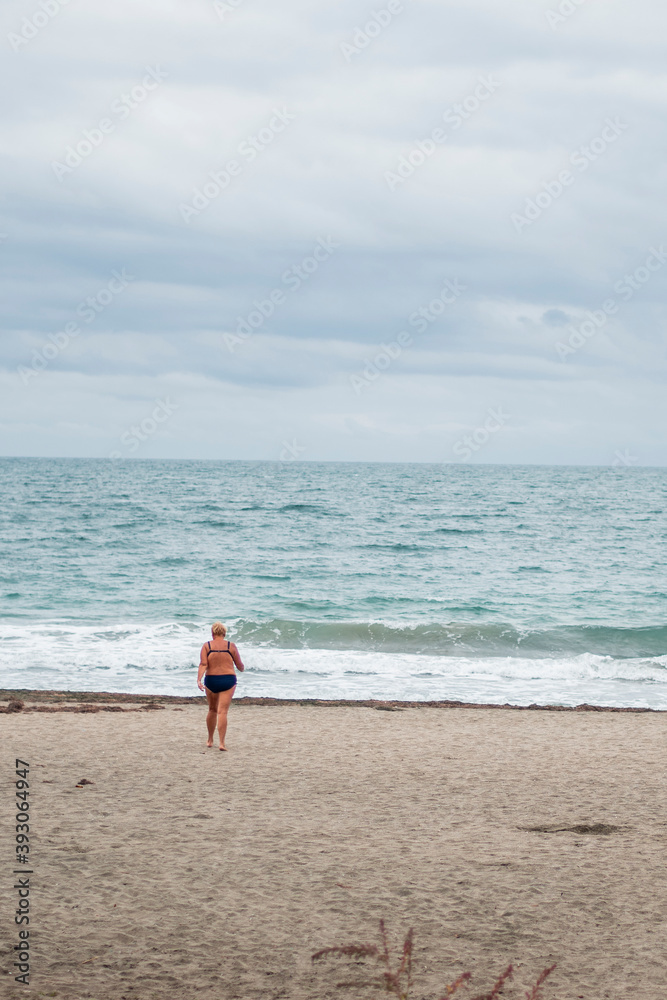 Obraz premium A woman going into the cold sea with her bathing suit on November 9-th 2020. Autumn winter season on the beach.