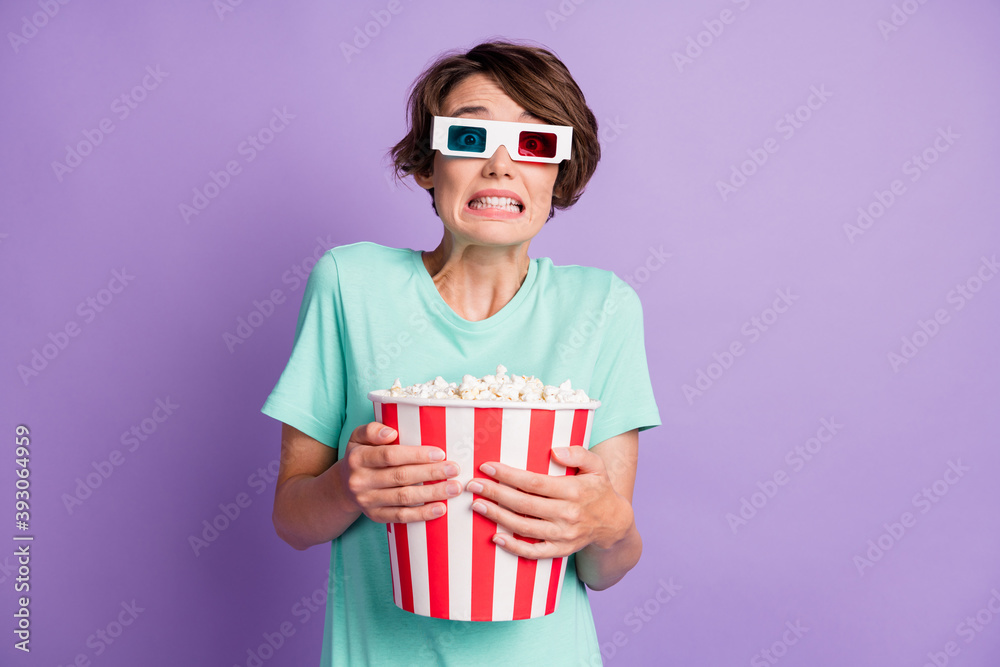 Photo of scared young woman dressed casual turquoise clothes 3d cinema eyeglasses holding popcorn bucket isolated violet color background Photo of scared young woman dressed casual turquoise clothes 3d cinema eyeglasses holding popcorn bucket isolated violet color background
