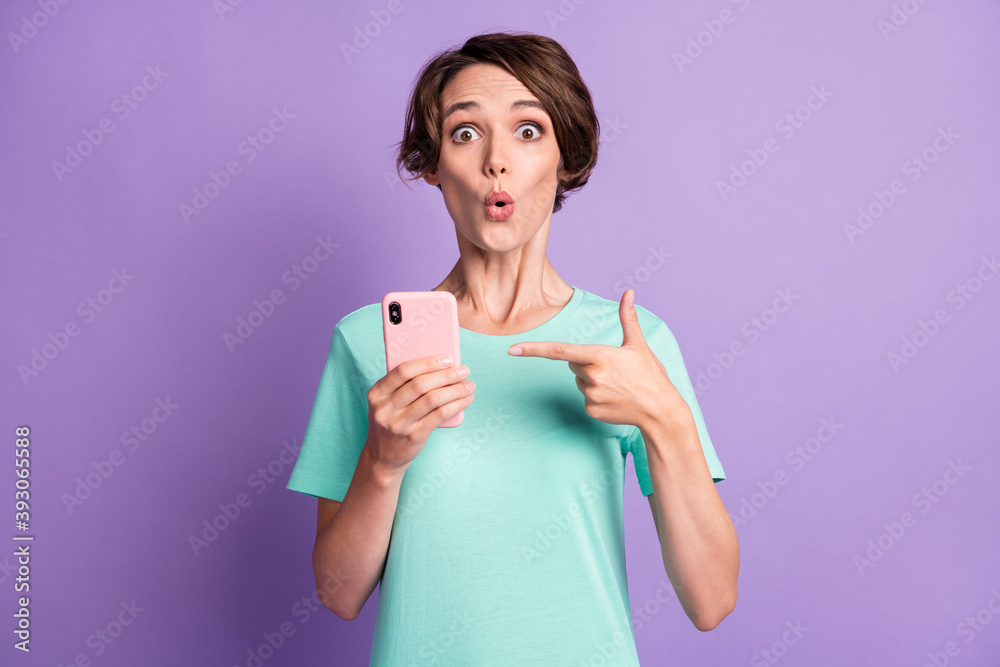 Photo of funny impressed young woman dressed casual turquoise clothes pointing phone isolated violet color background Photo of funny impressed young woman dressed casual turquoise clothes pointing phone isolated violet color background