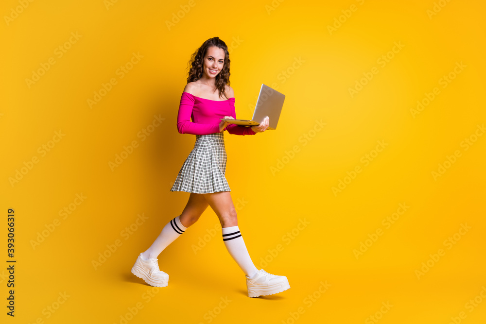Full length body size photo of busy female teenager keeping laptop smiling typing communicating going fast isolated on bright yellow color background Full length body size photo of busy female teenager keeping laptop smiling typing communicating going fast isolated on bright yellow color background